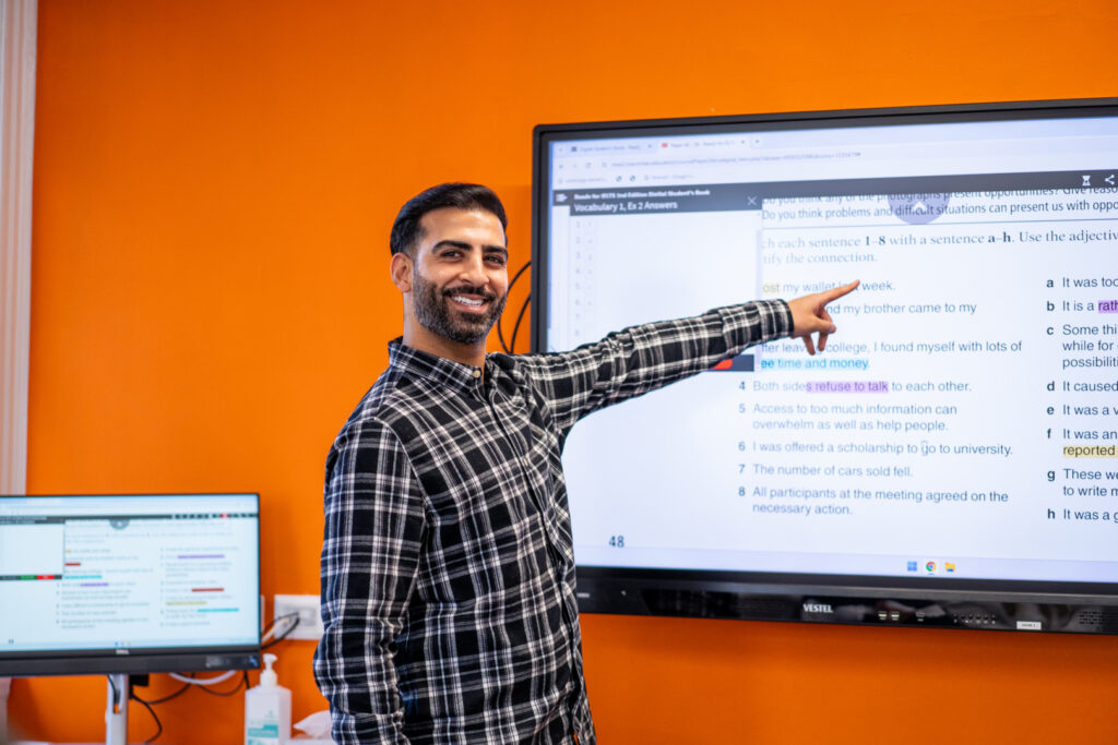 Teacher leading an interactive English lesson at EC English Cambridge using a digital classroom screen.