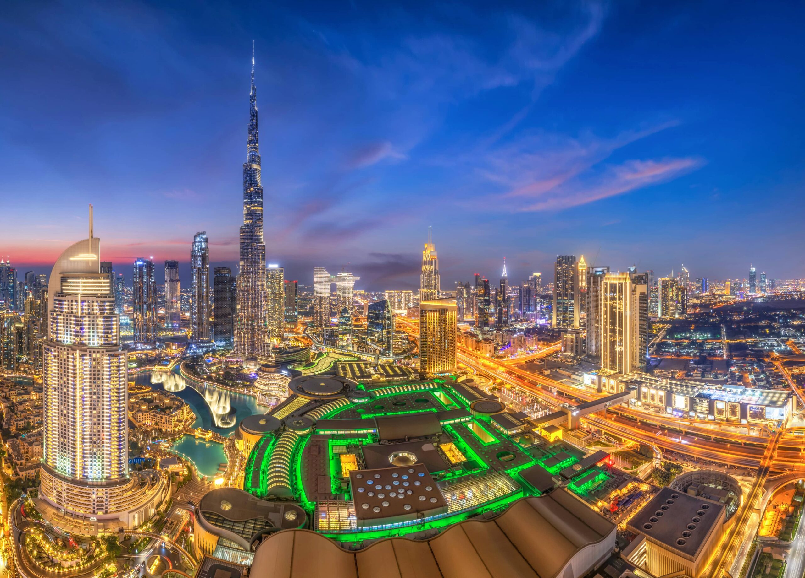 Skyline di Dubai al tramonto con il Burj Khalifa, grattacieli illuminati e il moderno quartiere finanziario della città.