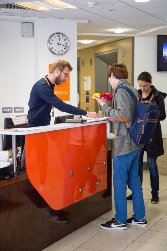 Studenti effettuano il check-in alla reception di EC English Brighton con l'assistenza di un membro dello staff.