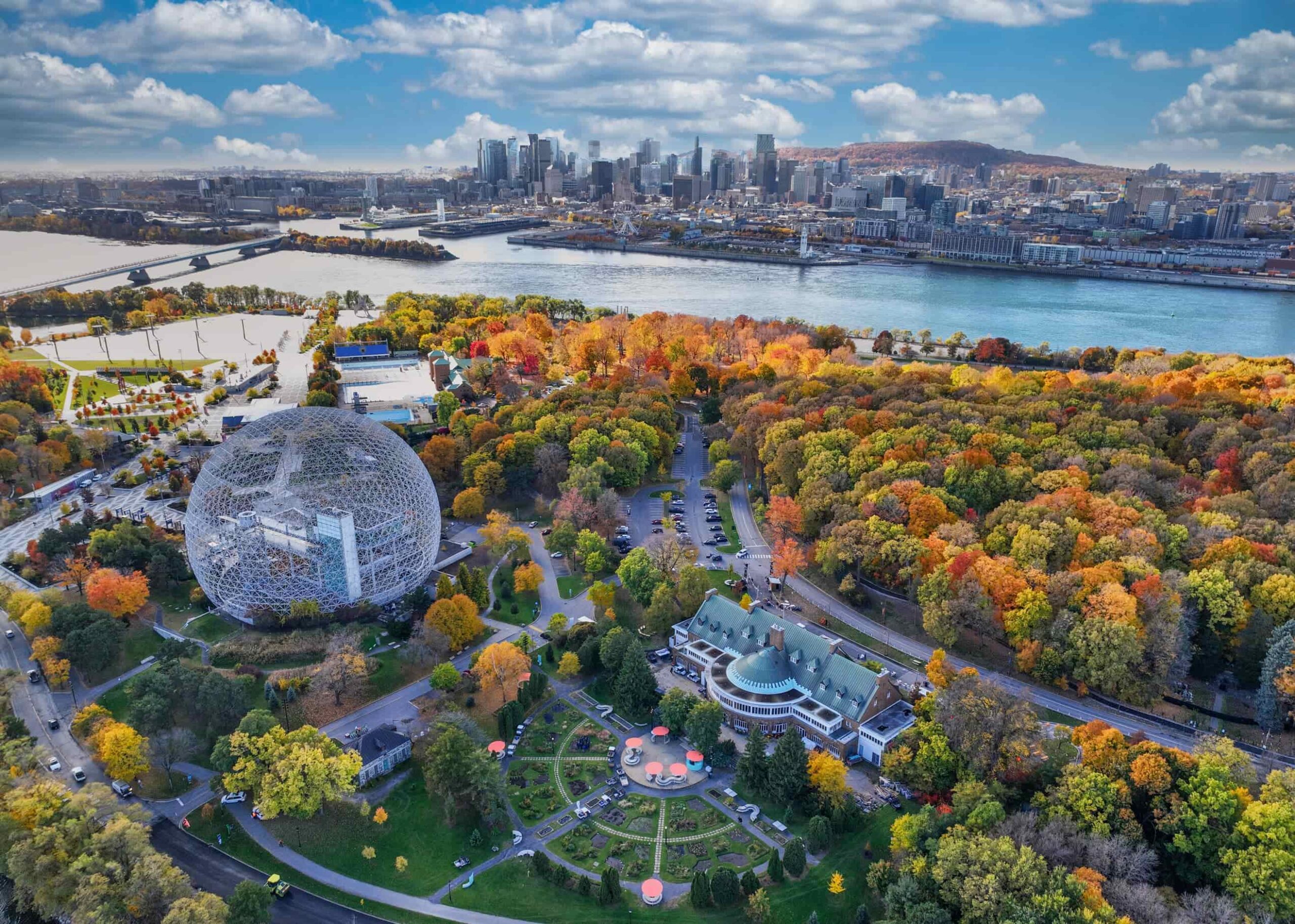 Vista a volo d'uccello di Montréal al tramonto con la Biosfera, il parco circostante e lo skyline della città sullo sfondo.