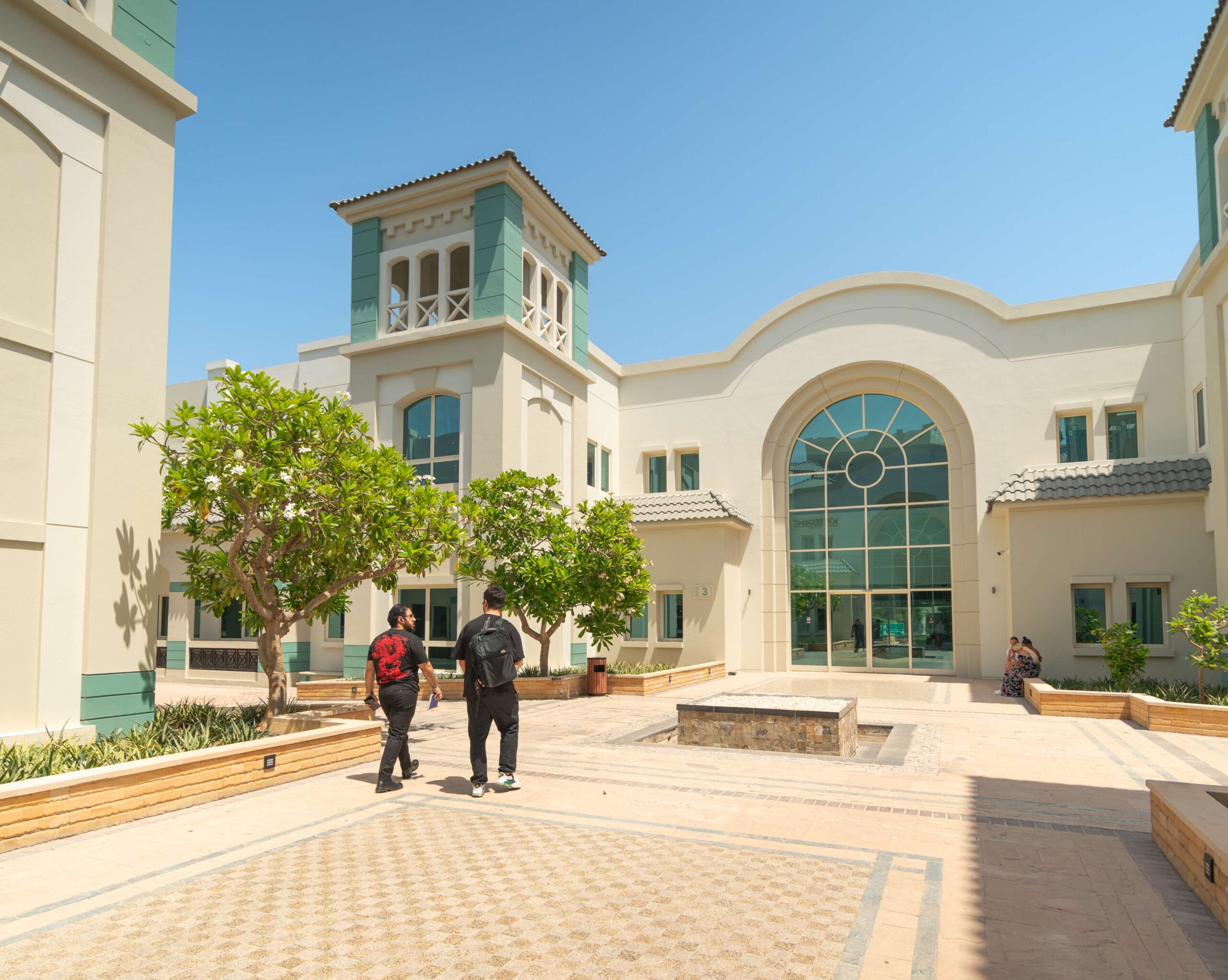 Vista esterna del moderno edificio della scuola di inglese EC Dubai con studenti che attraversano il cortile.