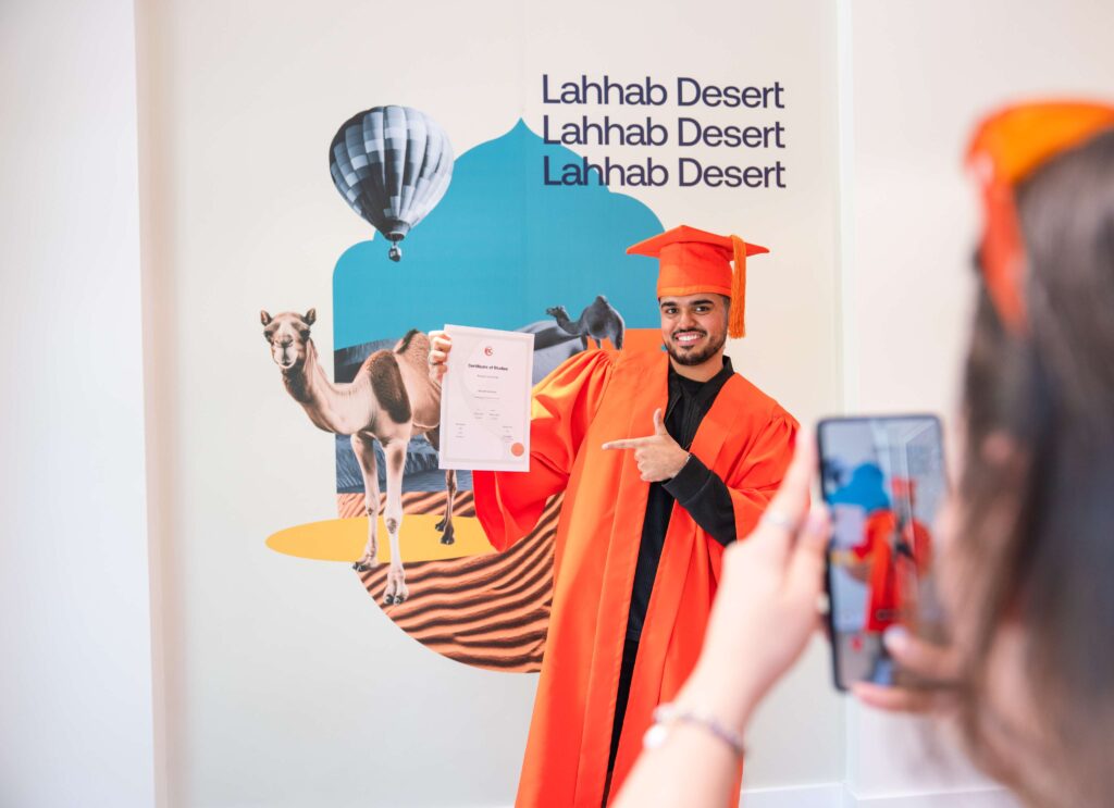 Studente di EC Dubai che celebra il diploma mostrando il certificato davanti a uno sfondo fotografico ispirato a Dubai.